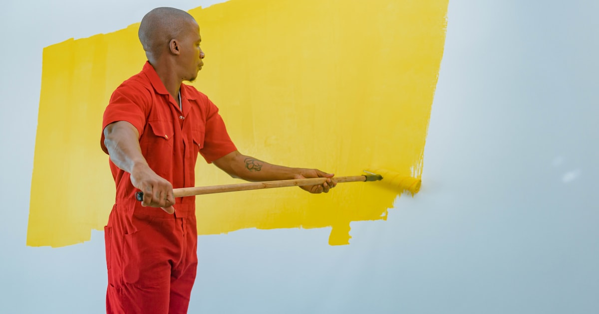 油漆師傅穿著紅色工作服正在用滾筒刷黃色油漆