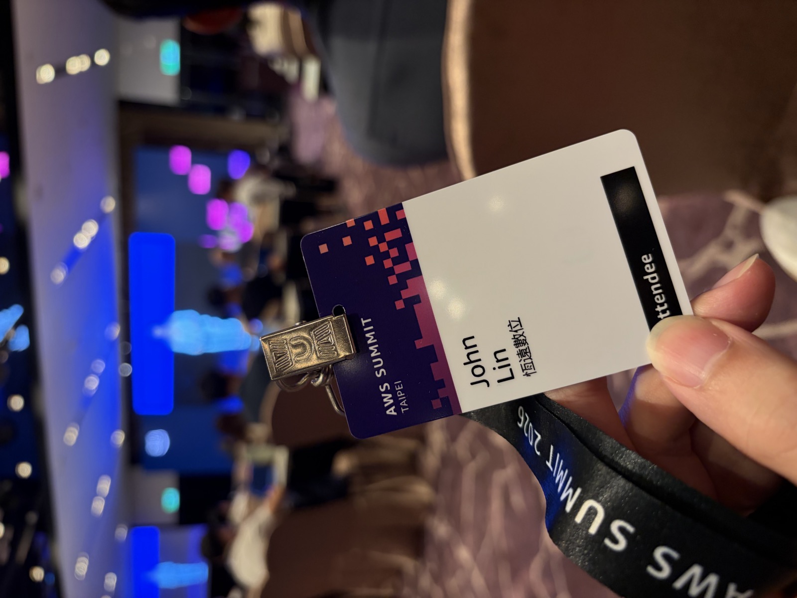 恆遠團隊成員手持 AWS Summit Taipei 2026 出席證，會場背景為研討會現場